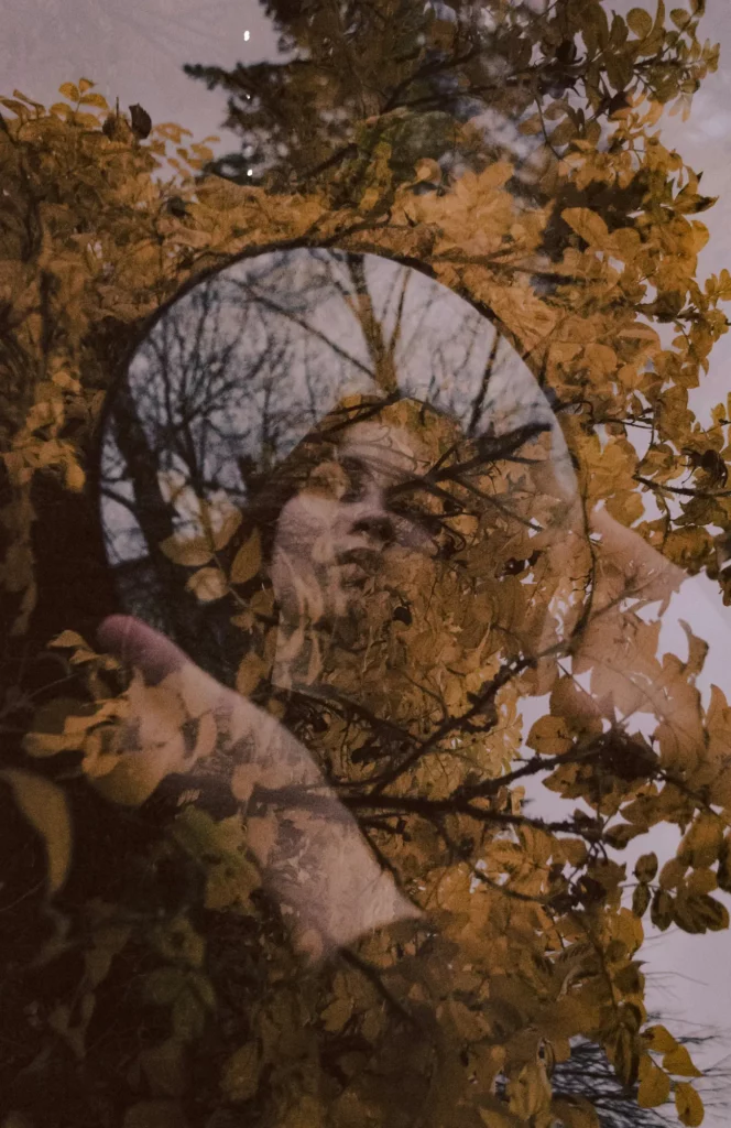 Visage de femme reflété dans un miroir rond parmi des feuillages d'automne